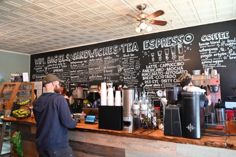 Adult, Male, Man, Person. Text: COFFEE iced house blend DARK ROAST black tea whoopass ROAST LIGHT chicken salad nutella ENGLISH BREAKFAST GREY EARL 16 20 iced 12 fresh daily PEACH OR GINGER &amp; cheese ANISE PHILLY DOUBLE SHOT! MEDIUM ROAST ALL DRINKS...