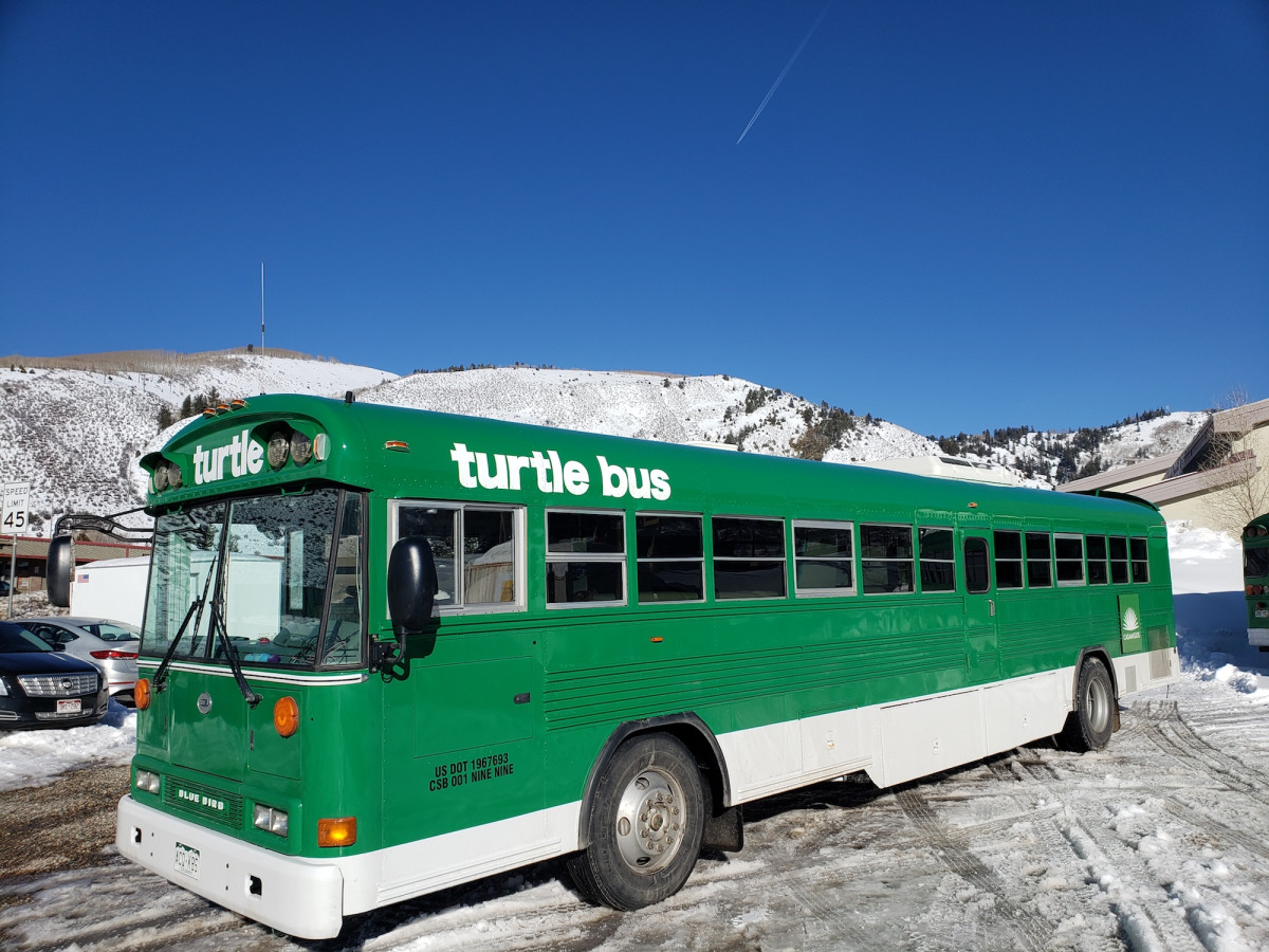 Bus, Vehicle, Car, Person. Text: turtle turtle bus SPEED LIMIT 45 US DOT 1967693 CSB 001 NINE NINE BLUE BIRD